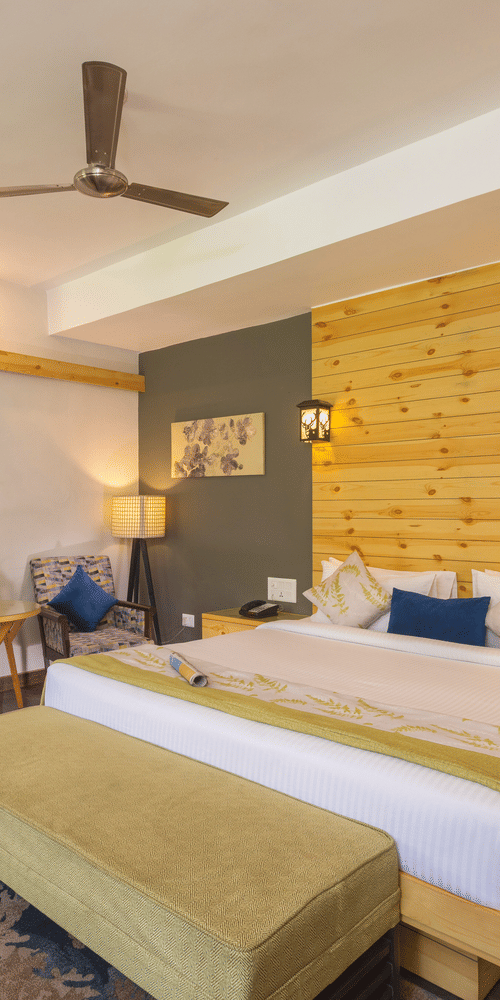 bedroom featuring a large bed with a decorative headboard, a seating area with chairs, and access to a balcony  at The Golden Tusk, Jim Corbett