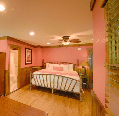 a brightly lit room with pastel pink colored walls featuring a double bed, wardrobe and a center table - Historic Tapoco Lodge