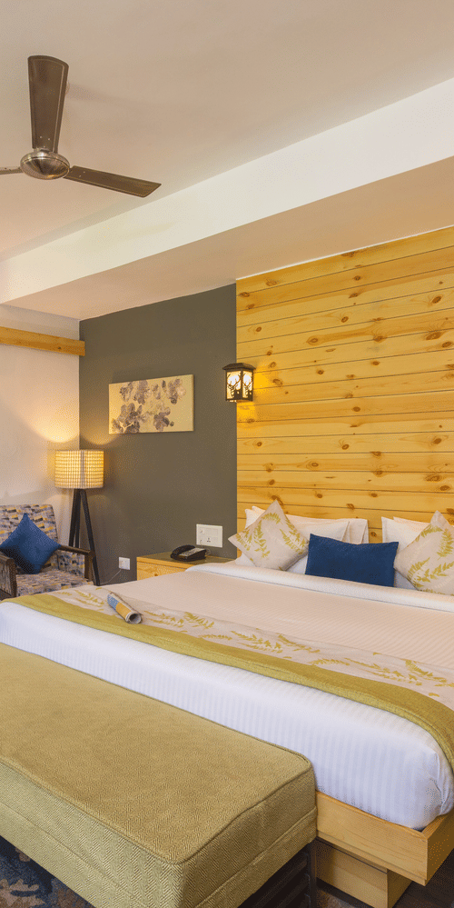 bedroom featuring a large bed with a decorative headboard, a seating area with chairs, and access to a balcony  at The Golden Tusk, Jim Corbett