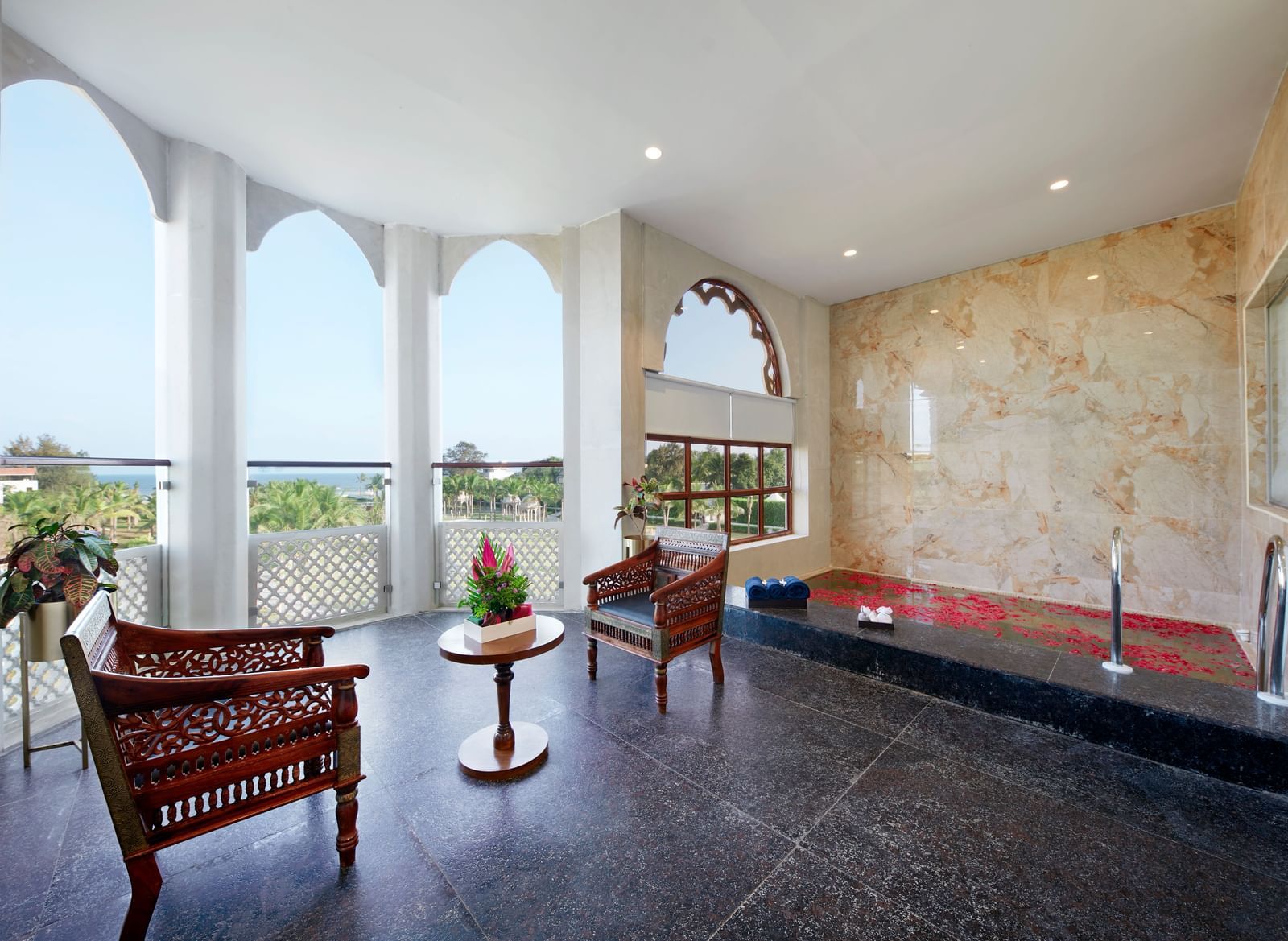 A balcony in the Executive Studio Villa featuring a seating area, a Jacuzzi with rose petals, and a panoramic view of the lush greenery surrounding the hotel - Kaldan Samudhra Palace