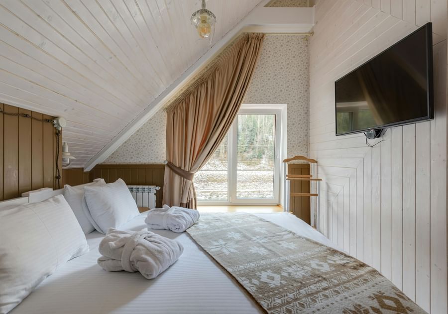 An attic-style room featuring twin beds with white linens on them and a wall-mounted TV.