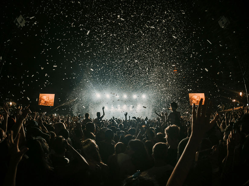 confetti flies in the air as people raise their hands and dance along to a concert
