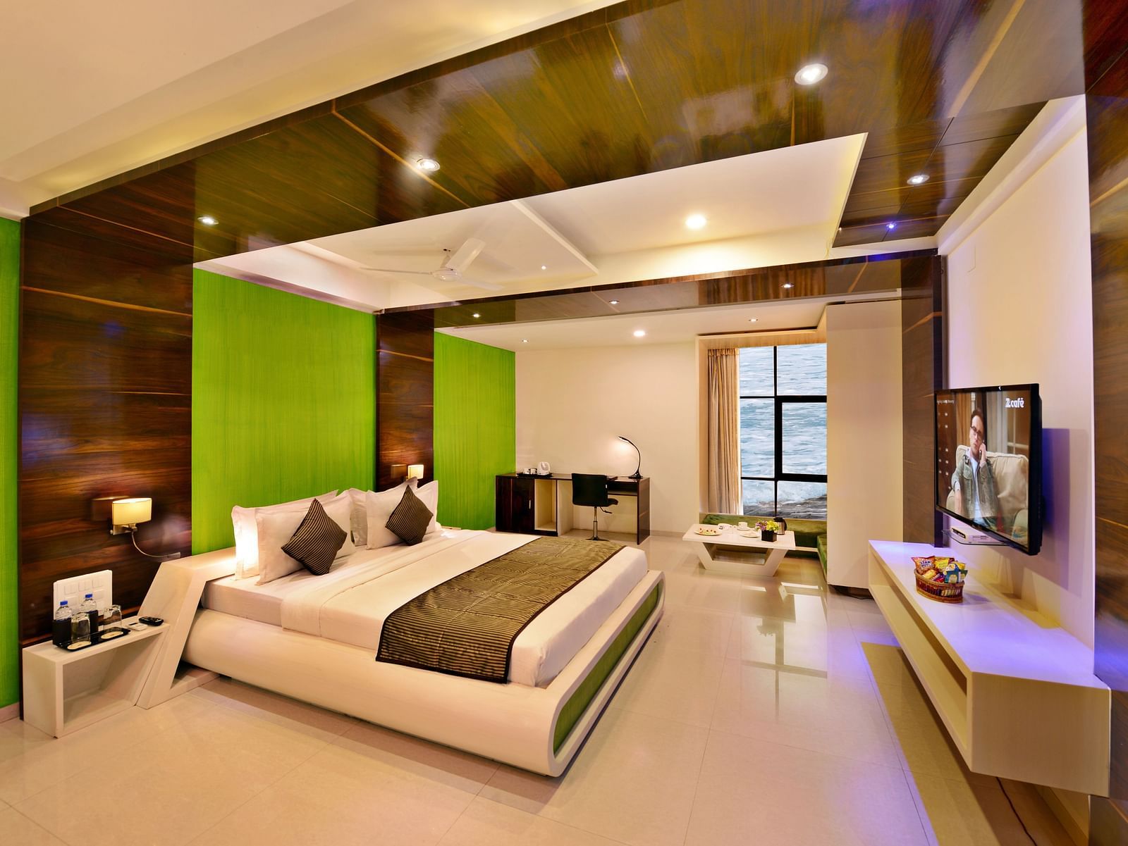 A contemporary hotel suite with a king size bed, green accent wall, and city view.