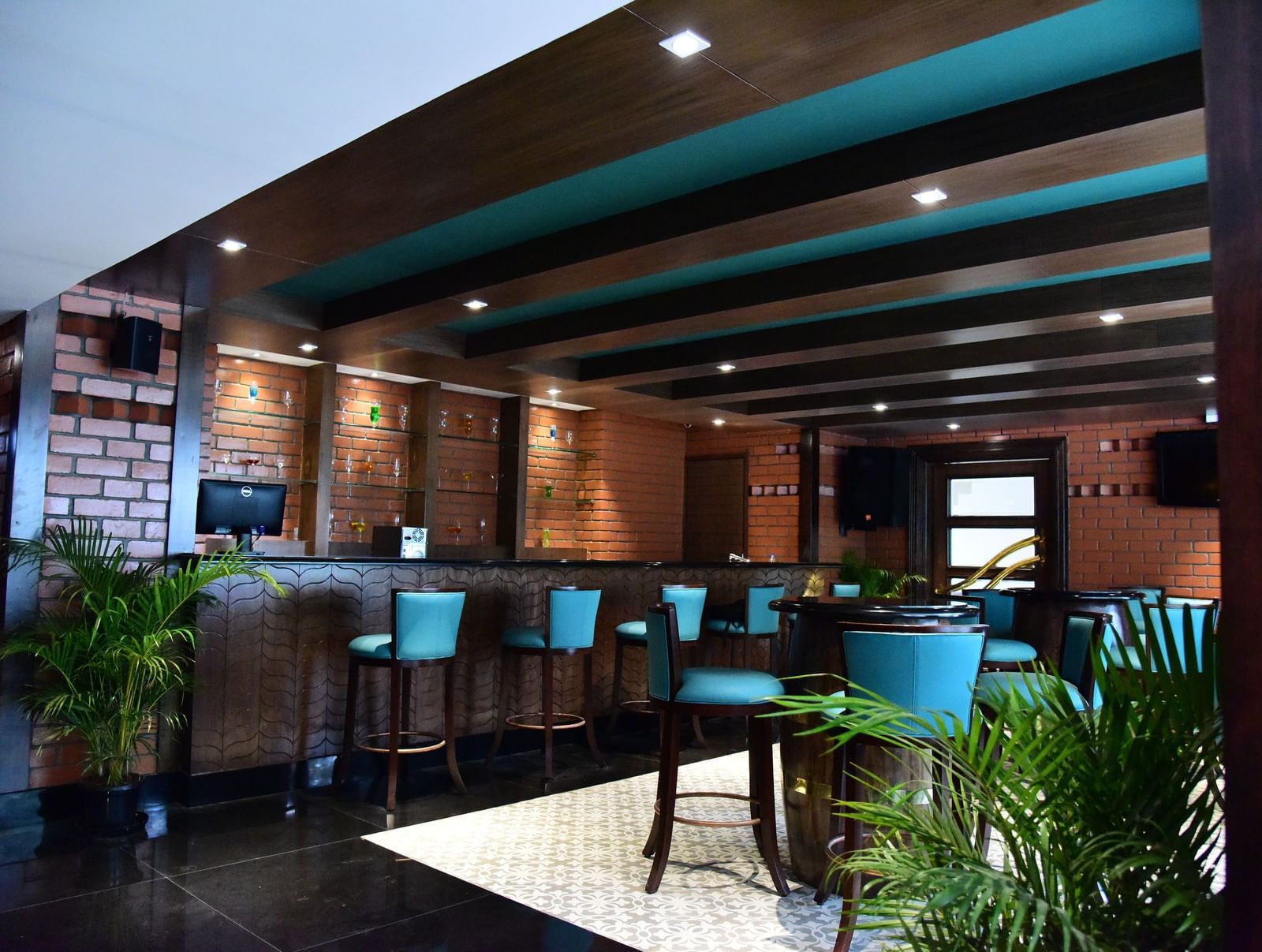 A vibrant hotel bar at The Royal Comfort, showcasing a brick-and-wood bar with bright blue-green stools and a warm, inviting ambience.