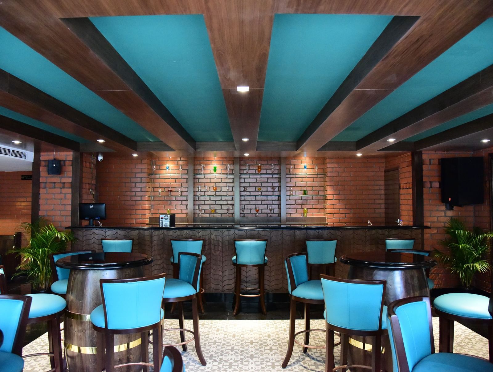 Another view of the bar at The Royal Comfort, highlighting the long wooden bar top, the brick wall behind it, and the stylish blue-green chairs.