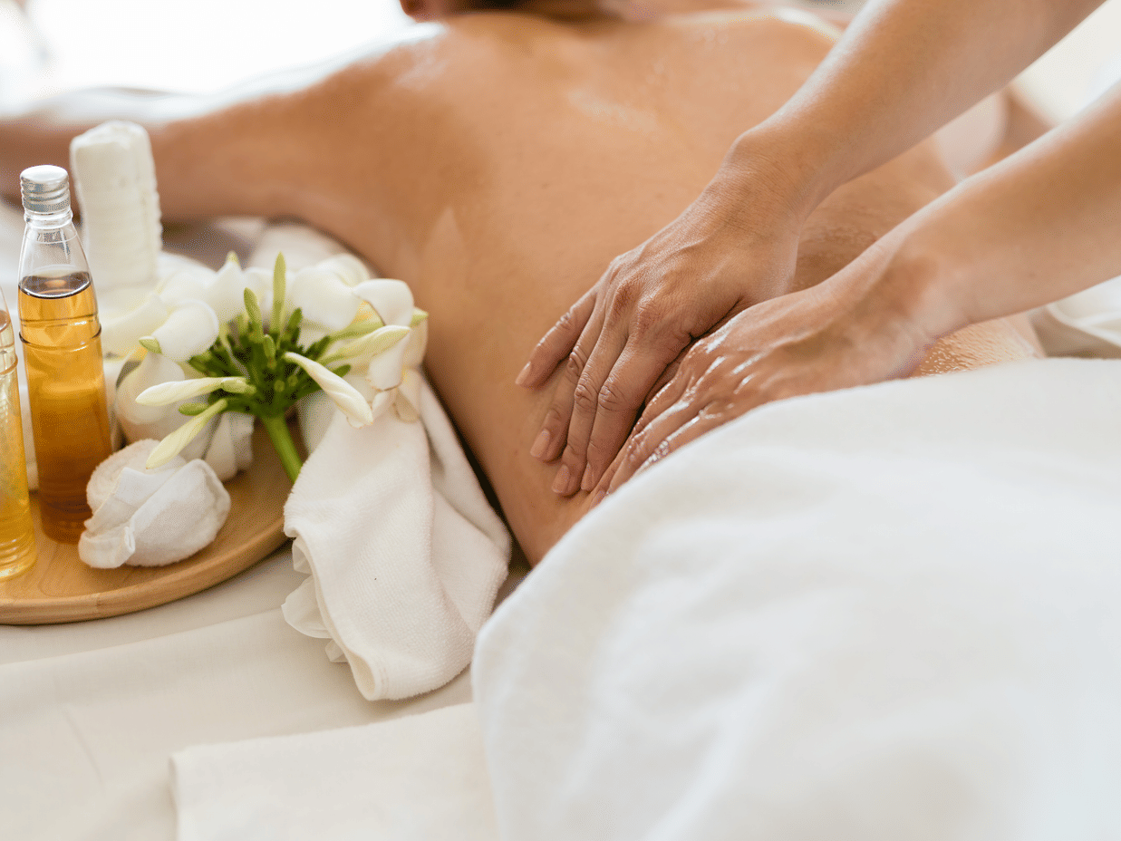 Therapist performing a deep back massage with essential oils and towels nearby.