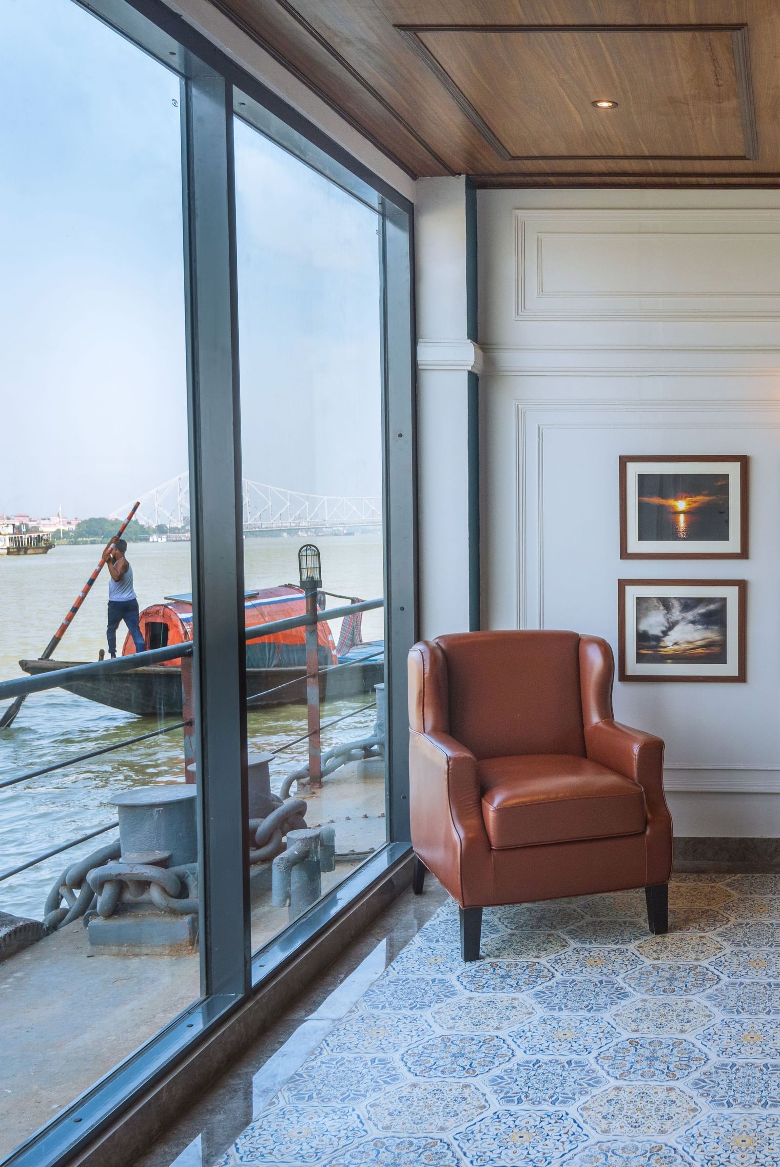 A Cosy seating area with wall art and river views through large glass windows at Polo Floatel Kolkata.