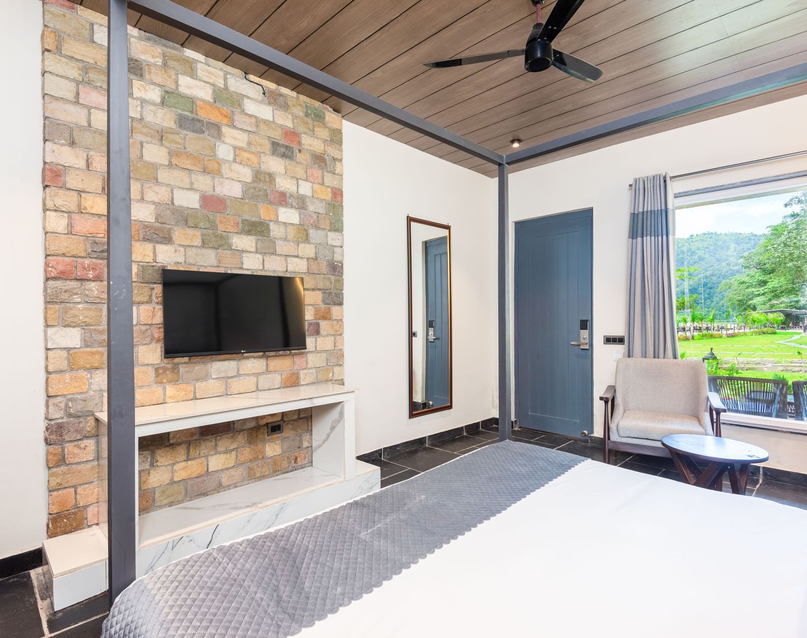 Closeup view of Luxury Cottage at DLS Divine River Resort and  Spa featuring a king size bed with mirror, TV and a chair.