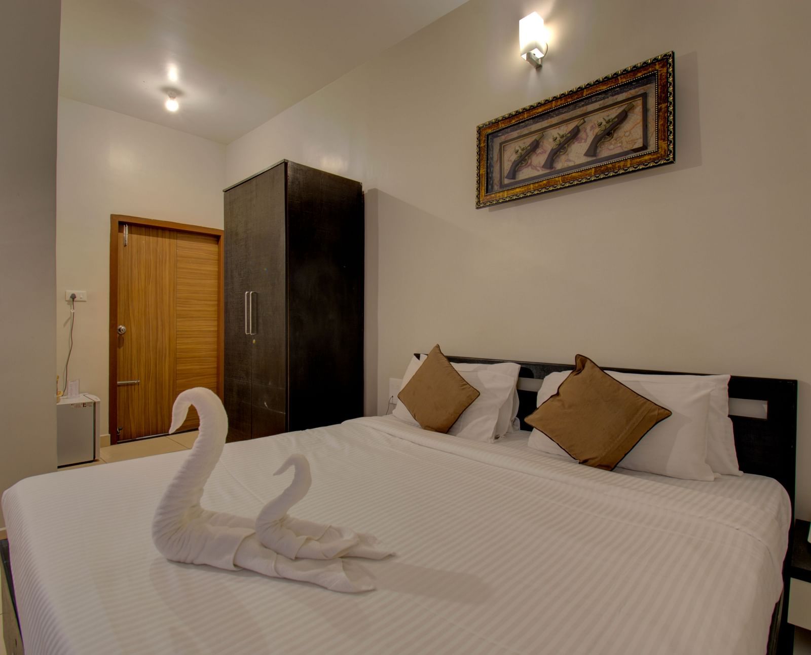 Swans made with towels on a huge bed, a cupboard, side table, a wall art and wooden door | Superior Room | Woodstock Resorts, Coorg