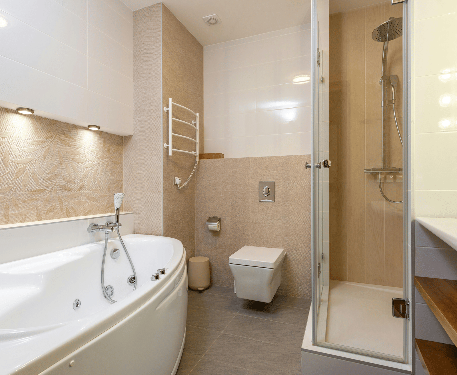 A bright, contemporary bathroom with a large, white corner bathtub, a toilet, a glass-enclosed shower, and warm under-cabinet lighting.