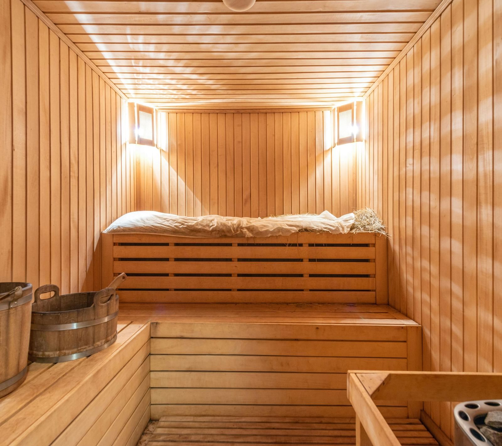 A wooden sauna room with two warm lights mounted in the corner of the ceilings.
