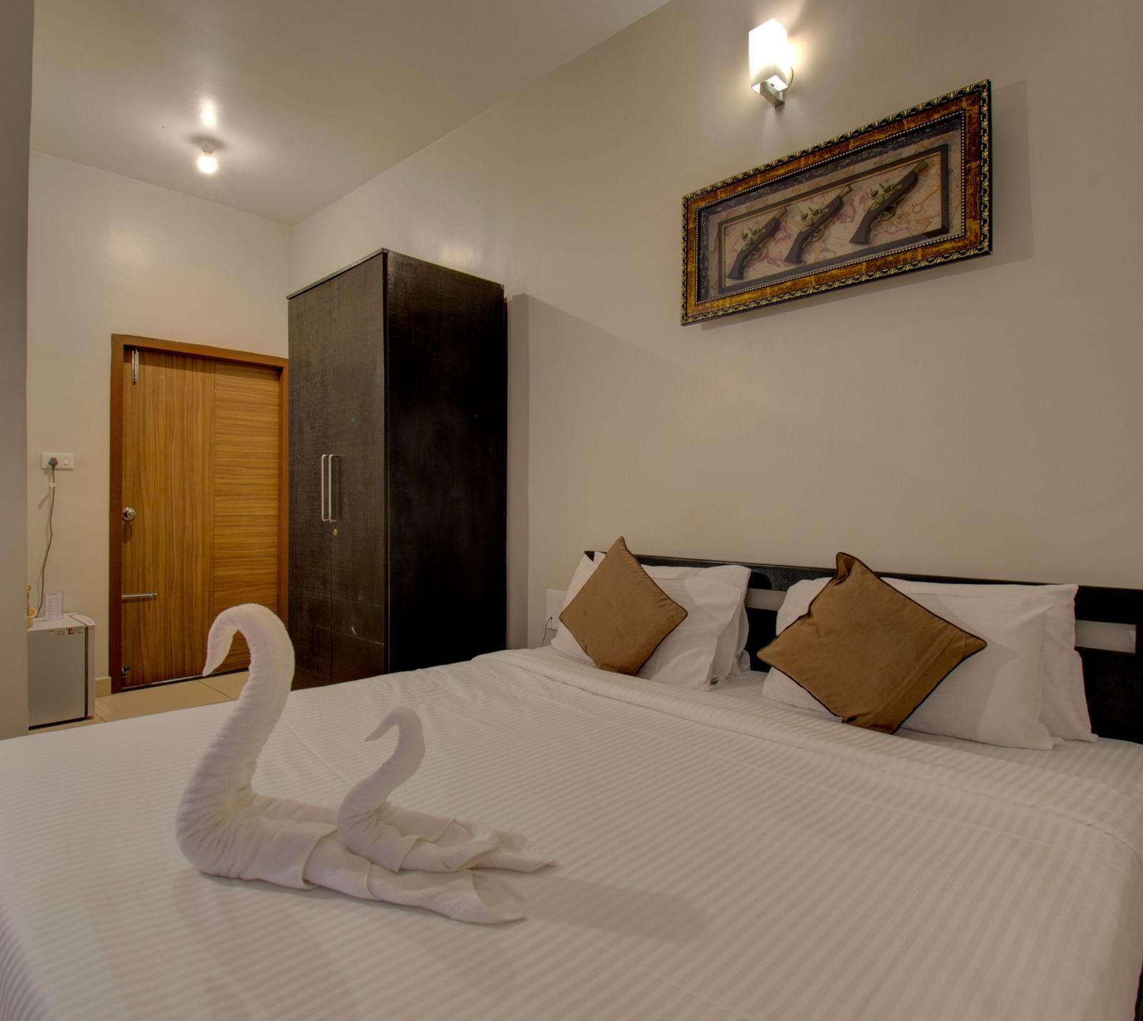 Swans made with towels on a huge bed, a cupboard, side table, a wall art and wooden door | Superior Room | Woodstock Resorts, Coorg