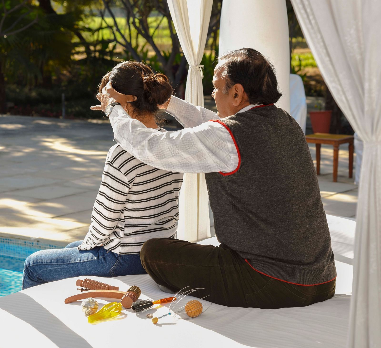 A man and woman seated on cushions, surrounded by various items and draped fabric- Shahpura Bagh.