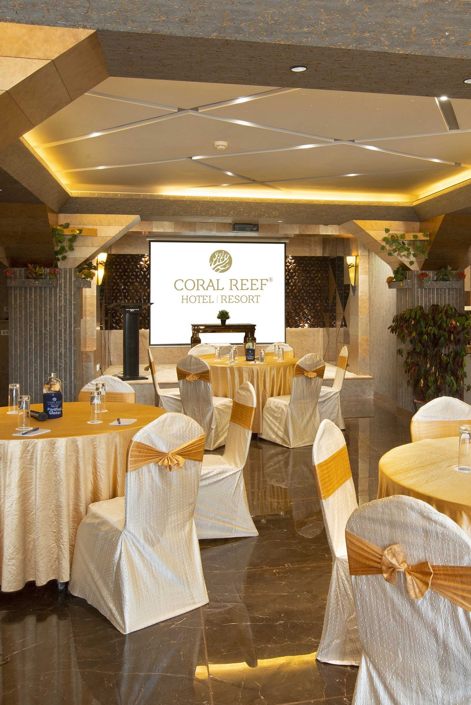 Image of tables arranged along with chairs in circles and a projector screen in the background at Mosaic Hall at Coral Reef Hotel and Spa in Port Blair