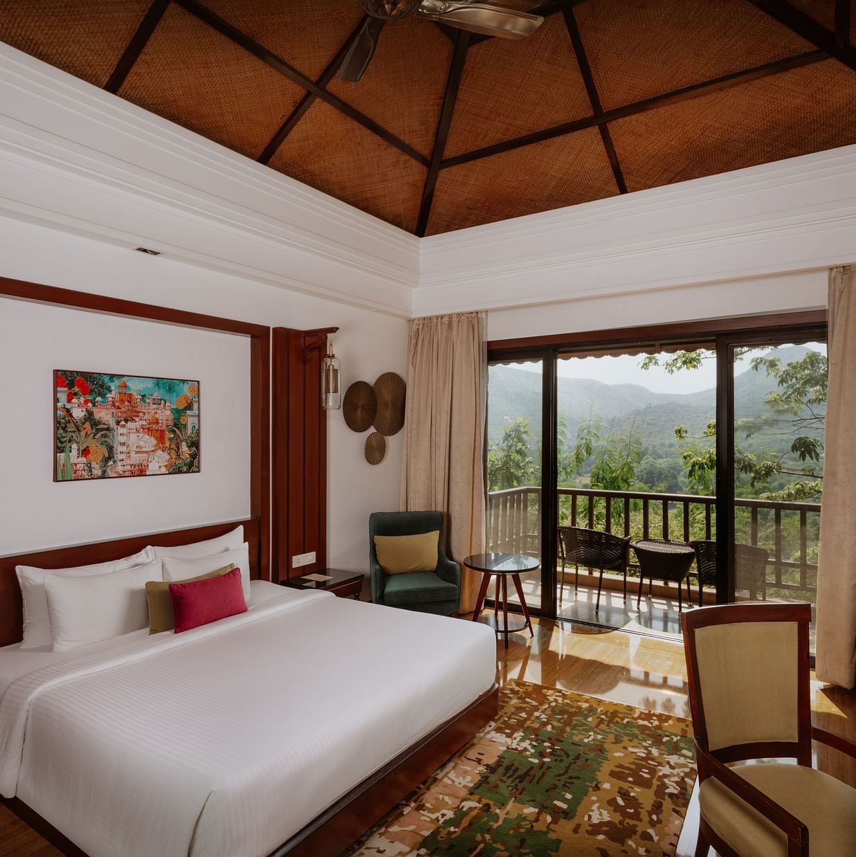 Corner view of the Luxury Villa bedroom at The Ananta, Udaipur, featuring a spacious balcony with scenic views, and a flat-screen TV, seating area with chair and a working desk.