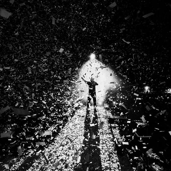 An outdoor concert, with the lead singer under white spotlight and white paper shreds floating in the air.