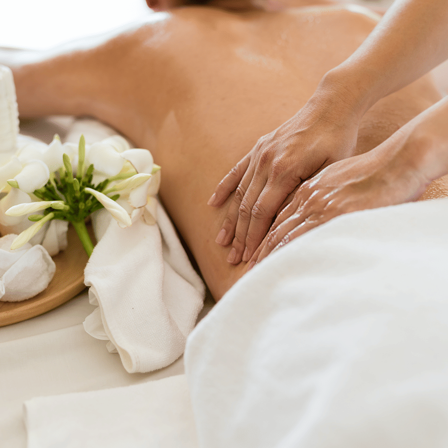 Therapist performing a deep back massage with essential oils and towels nearby.