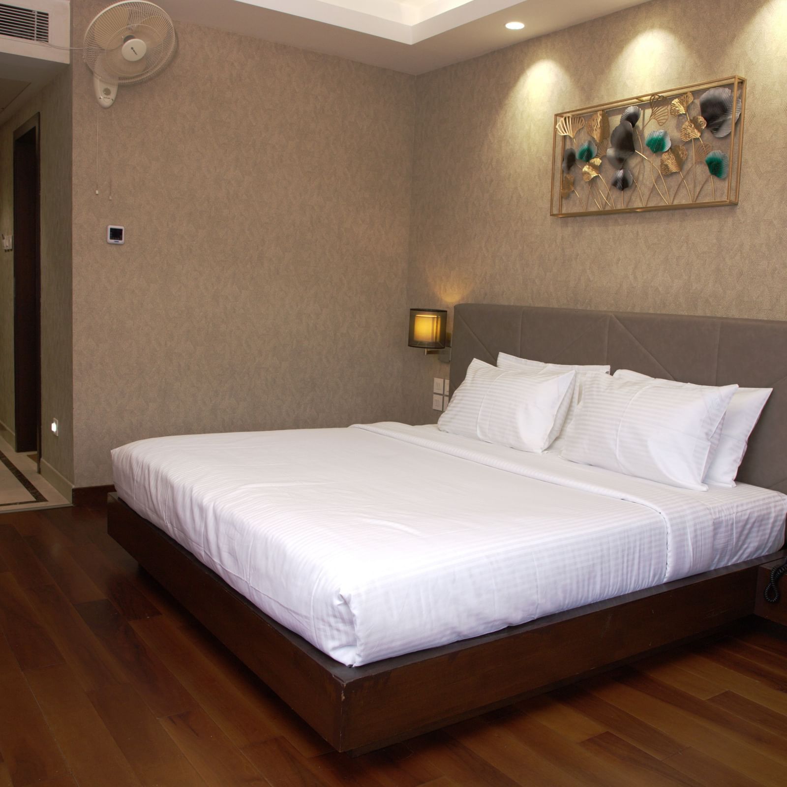 A spacious bedroom with a large bed, wall art above the headboard, bedside lamps, and wooden flooring at The Hamuse Hotel, Kodaikanal.