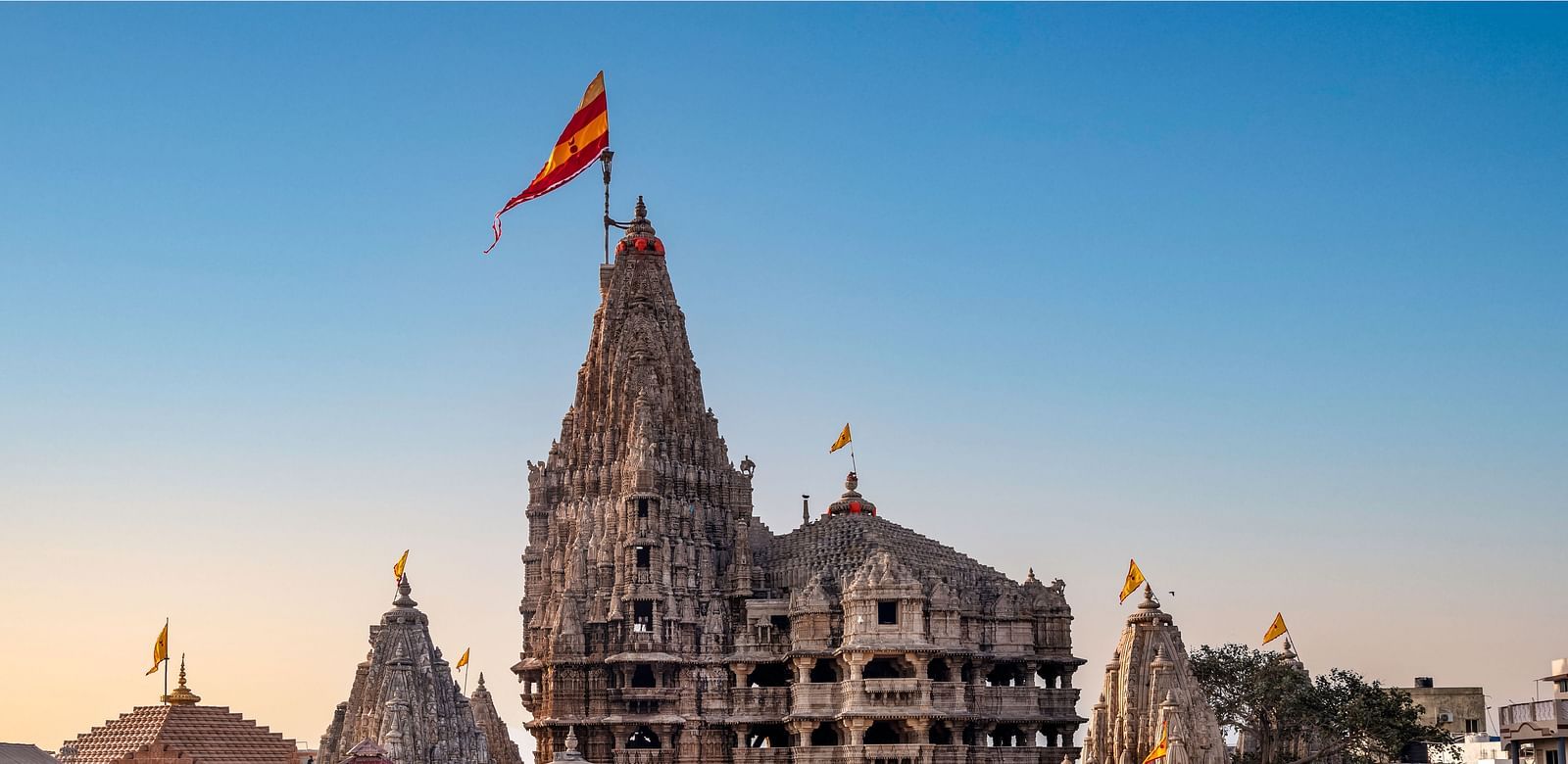 The intricately carved spires and orange flag of the Dwarkadhish Temple in Dwarka, Gujarat, under a clear sky.