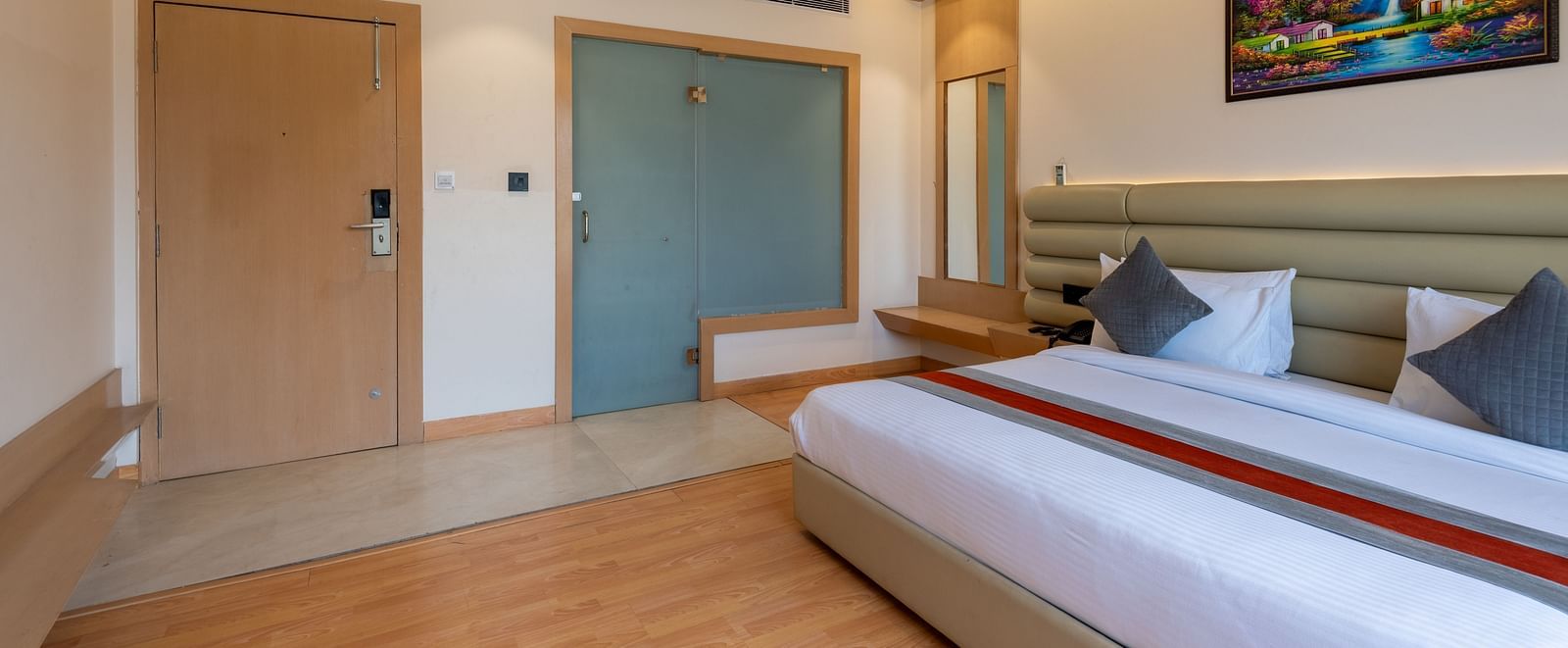 A king size bed in a room along with bed side tables, a full length mirror and other amenities - DLS Hotel Arihant. Haridwar