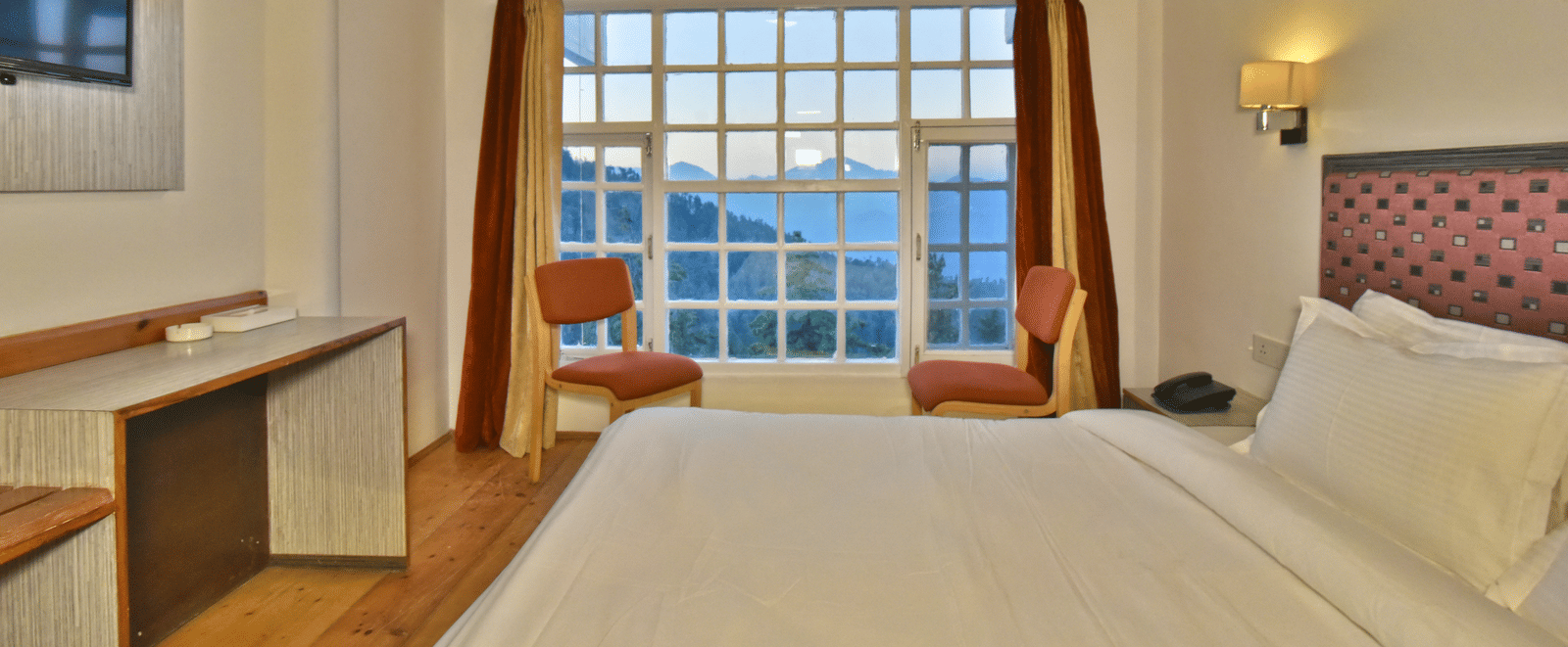 A bedroom with large windows, showcasing natural light through open curtains at DLS Hillcrest Resort, one of the best places to stay in Mashobra.