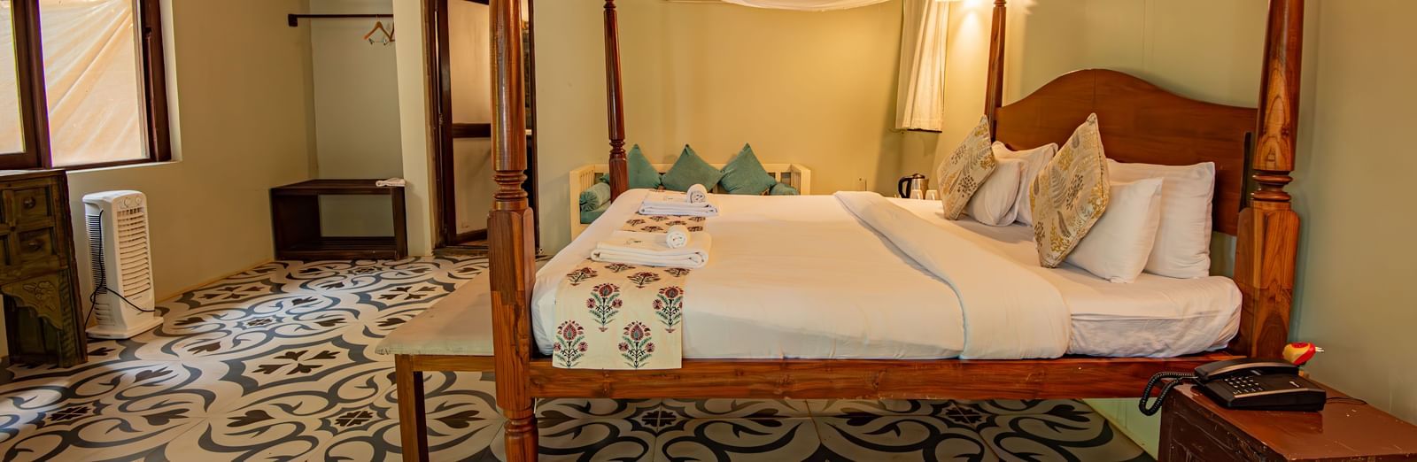 Side view of the spacious room with a large bed, bedside wooden table, and wooden-panelled ceiling at De Soul Santé, Morjim.