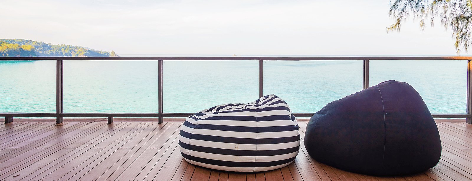 A deck with 2 bean bag seats facing the ocean, with a railing and clear sky in the background.