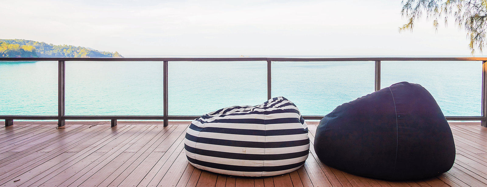 A deck with 2 bean bag seats facing the ocean, with a railing and clear sky in the background.