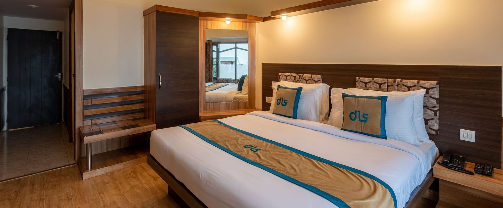 Deluxe room with wooden flooring, a mirror, a wardrobe, and a bedside table with a fan and comfortable bedding - DLS Meghavan Resort, Dharamshala