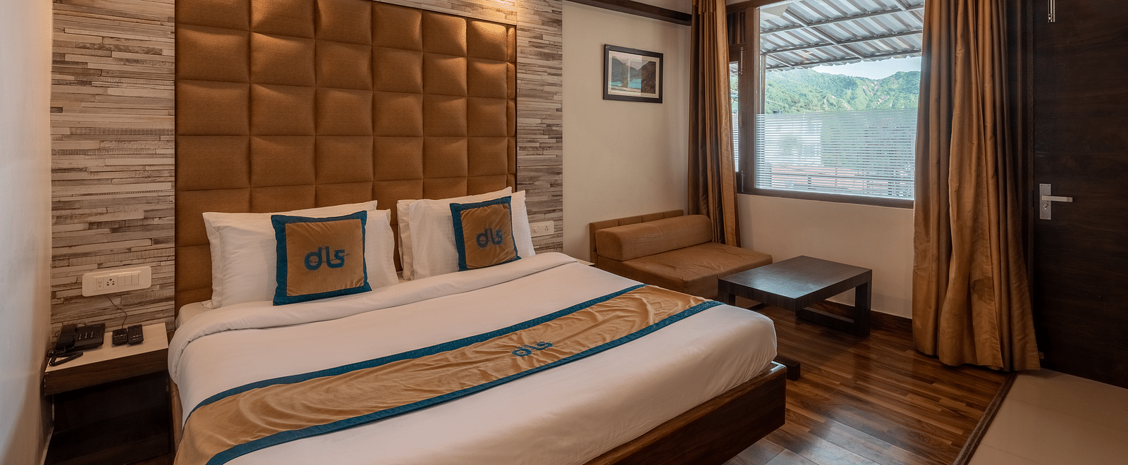 Deluxe room with a wooden accent wall, fan, and a seating area by the window with mountain views - DLS Meghavan Resort, Dharamshala