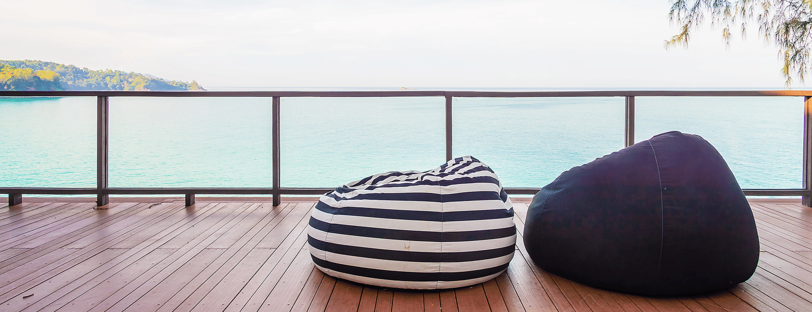 A deck with 2 bean bag seats facing the ocean, with a railing and clear sky in the background.