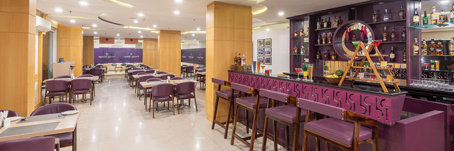Restaurant dining area with tables, chairs and a bar counter in the background at Mango Grove Hotel.