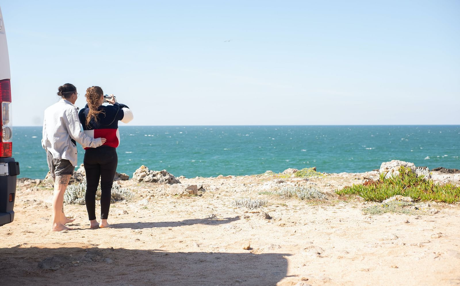 a couple taking pictures of the beach during the daytime
