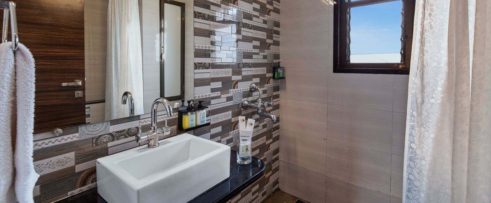 Stylish bathroom at Mayur Retreat with stone-textured wall, white basin, and vanity mirror.