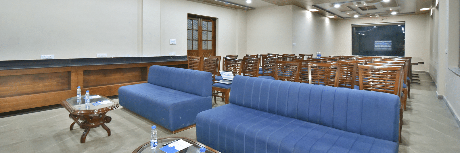 A banquet hall with a blue sofa and wooden chairs facing the podium at DLS Ark Holiday Inn, Banikhet.