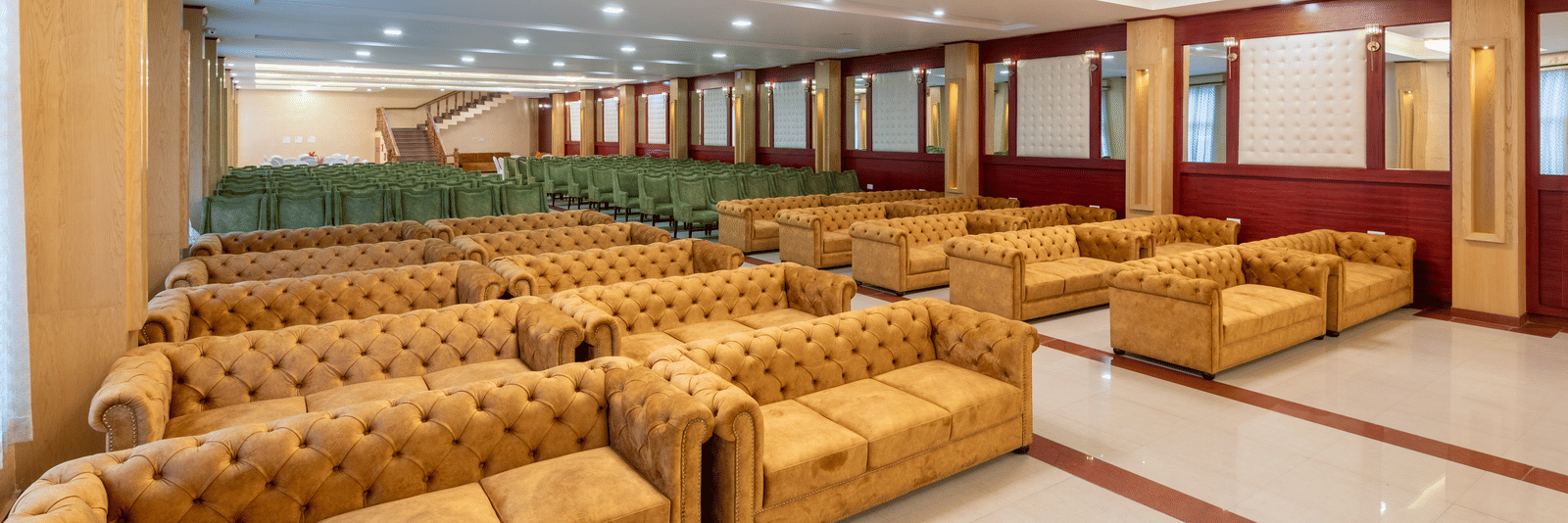 A spacious DLS Hotels banquet hall featuring rows of tufted sofas and polished flooring for large events.