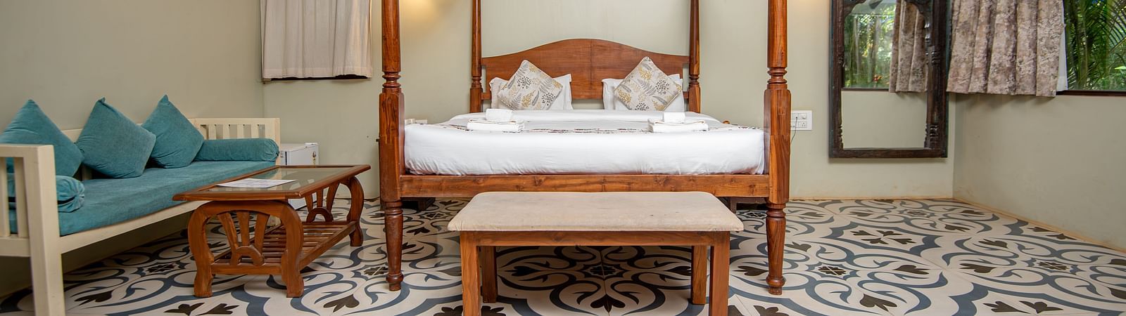 Spacious guest room with two sofas and a canopy bed under a sloped wooden roof at De Soul Santé, Morjim.