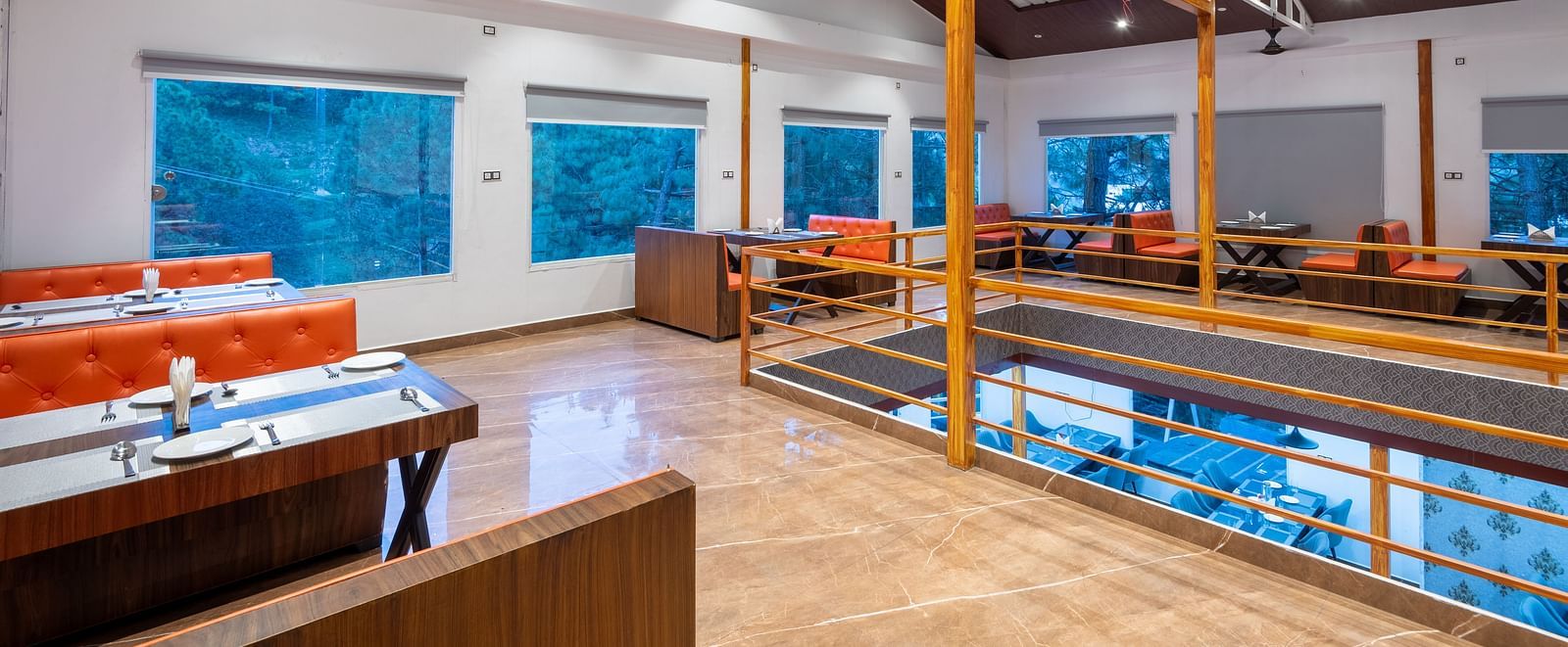 Modern restaurant interior with wooden furniture, orange seating, large windows, and ceiling lights - DLS Nature Trinket Resort, Dalhousie.