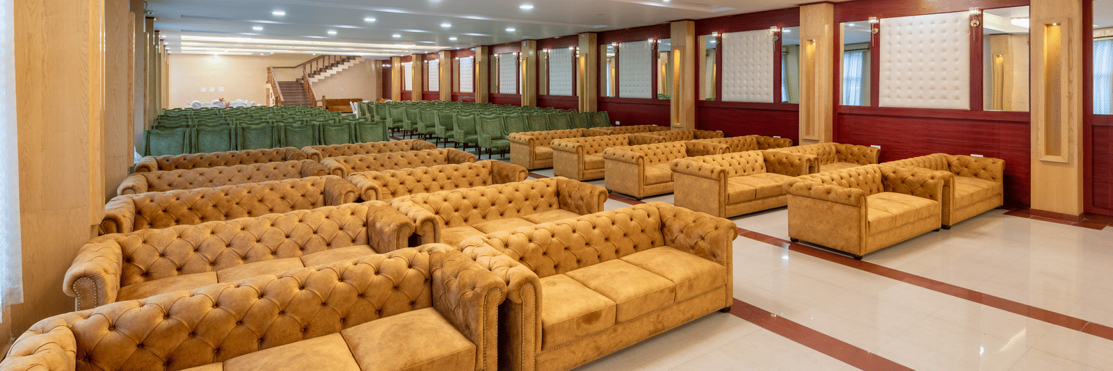 A spacious DLS Hotels banquet hall featuring rows of tufted sofas and polished flooring for large events.