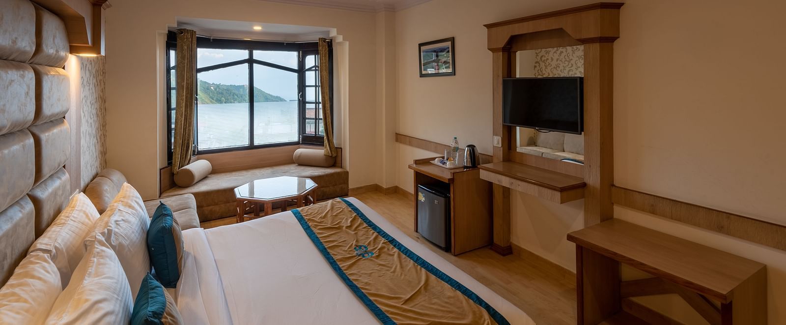 A premium room with a comfy bed, wooden accents, a flat-screen TV, and scenic window views, offering a relaxing and spacious stay - DLS Meghavan Resort, Dharamshala