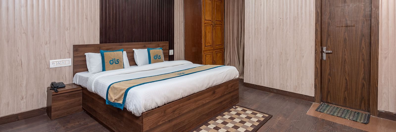 A wide angle shot of a king size bed in the a room with wooden flooring  | DLS Anupam Resort, Dharamshala