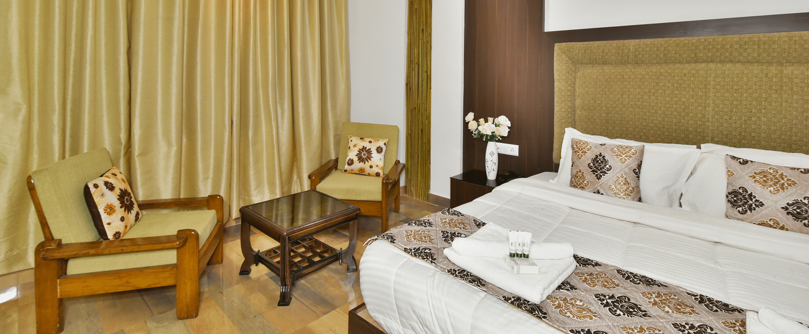 A side angle shot of a room that showcases the king size bed and the cosy seating arrangement | DLS Kapoor Resort Manali
