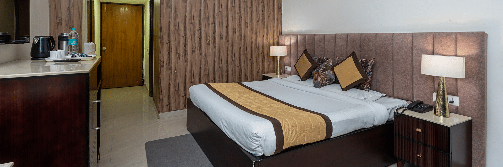 The image shows a hotel room with a large bed, two nightstands, a dresser, and a TV. There is also a door | DLS The Pearl