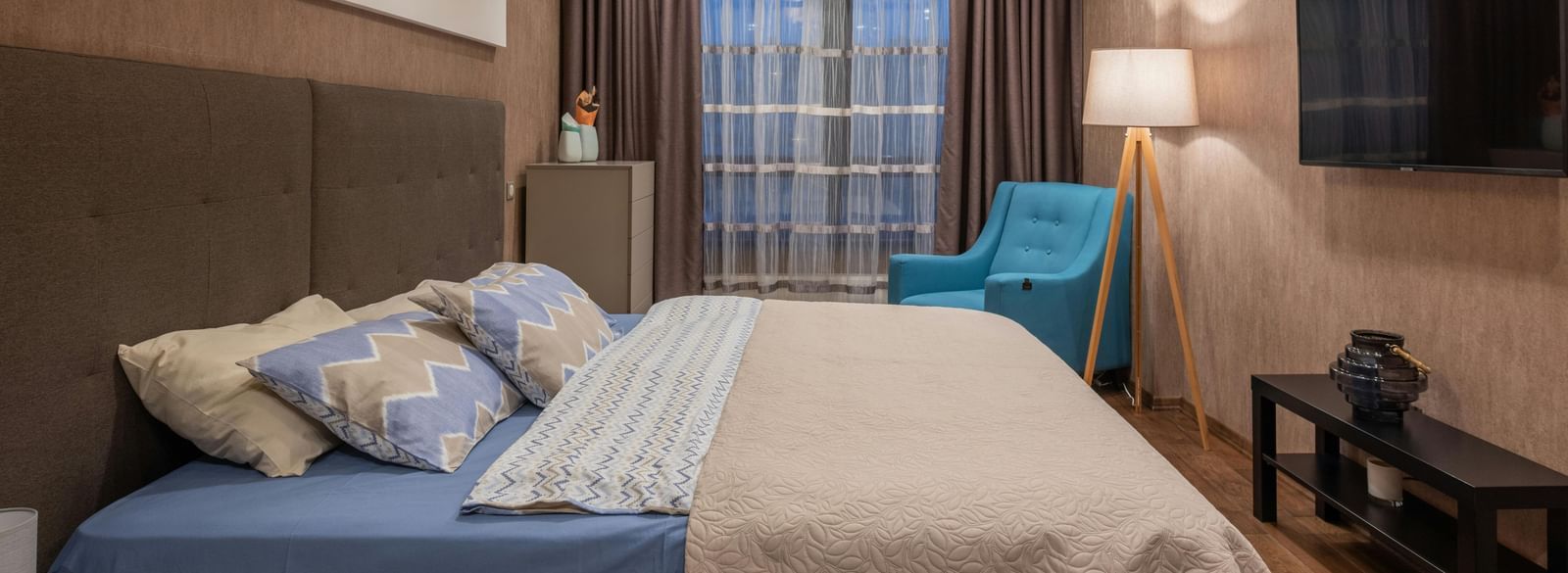 Cosy hotel room with large bed, soft lighting, modern decor, and a wall-mounted TV