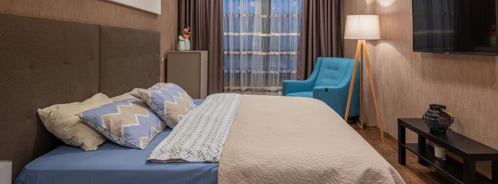 Cosy hotel room with large bed, soft lighting, modern decor, and a wall-mounted TV