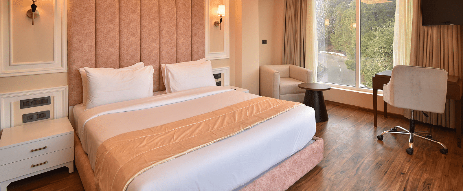 A modern hotel room with a king-sized bed, featuring soft lighting and large windows that offer stunning views of the surrounding hills and landscape.
