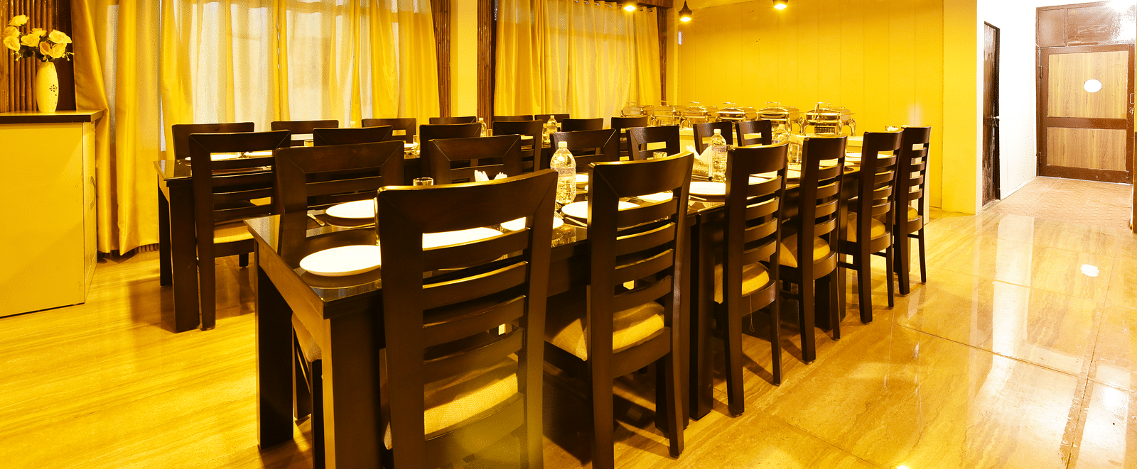 A shot of the dining table at the restaurant featuring woodden tables and chairs | DLS Kapoor Resort Manali