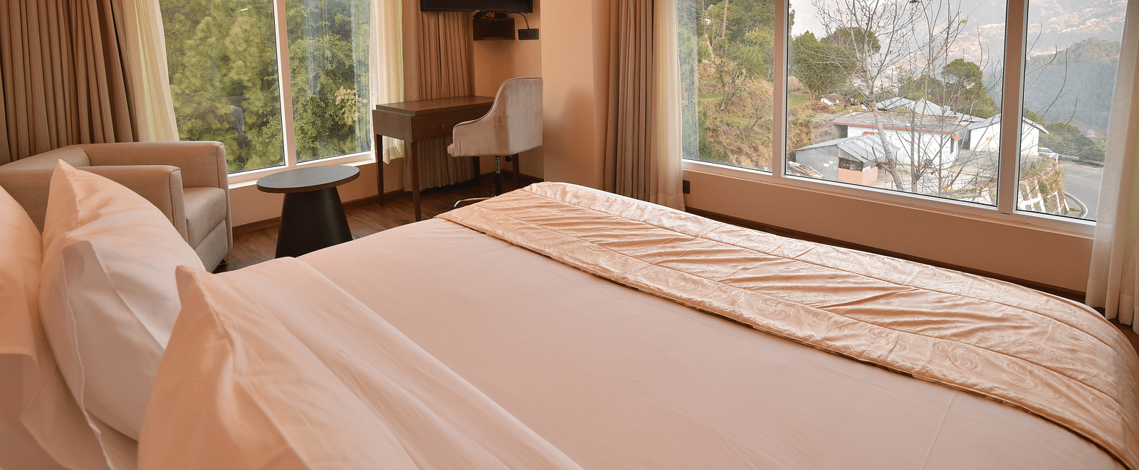 A well-lit bedroom with contemporary decor, large windows, and a comfortable bed. The space offers a calm, serene environment with views of the mountains.
