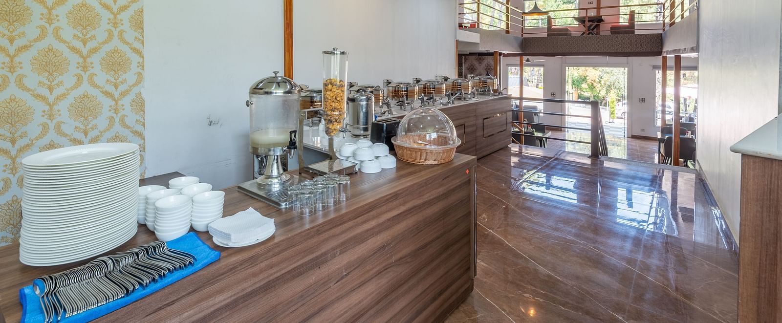 Restaurant buffet counter with serving containers, utensils, and modern decor featuring wood finishes and patterned wallpaper - DLS Nature Trinket Resort, Dalhousie.