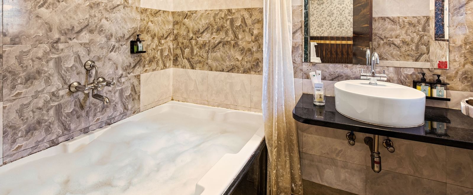 Modern bathroom at Mayur Retreat with a bathtub, stone-textured walls, and a large mirror.